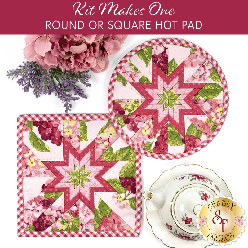 The two completed Folded Star Hot Pads, colored in blush pink florals fabrics from the Hydrangeas in the Garden collection by Riley Blake Designs, staged on a white table with coordinating floral décor and a teapot.