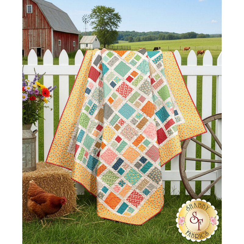 The Charming Charlie quilt in bright yellow, teal, pink, and orange fabrics from the Farmer's Daughter collection, draped over a white picket fence in front of a barn, with coordinating décor and a chicken in the foreground. A gold Shabby Fabrics logo is in the bottom right corner of the image.