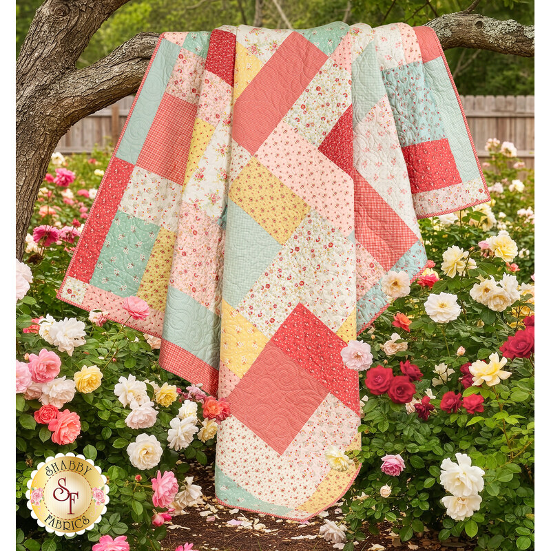 The completed Turning Twenty quilt, colored in the Lyda Rose collection by Moda, hung on a tree branch surrounded by multi-colored rose bushes. 