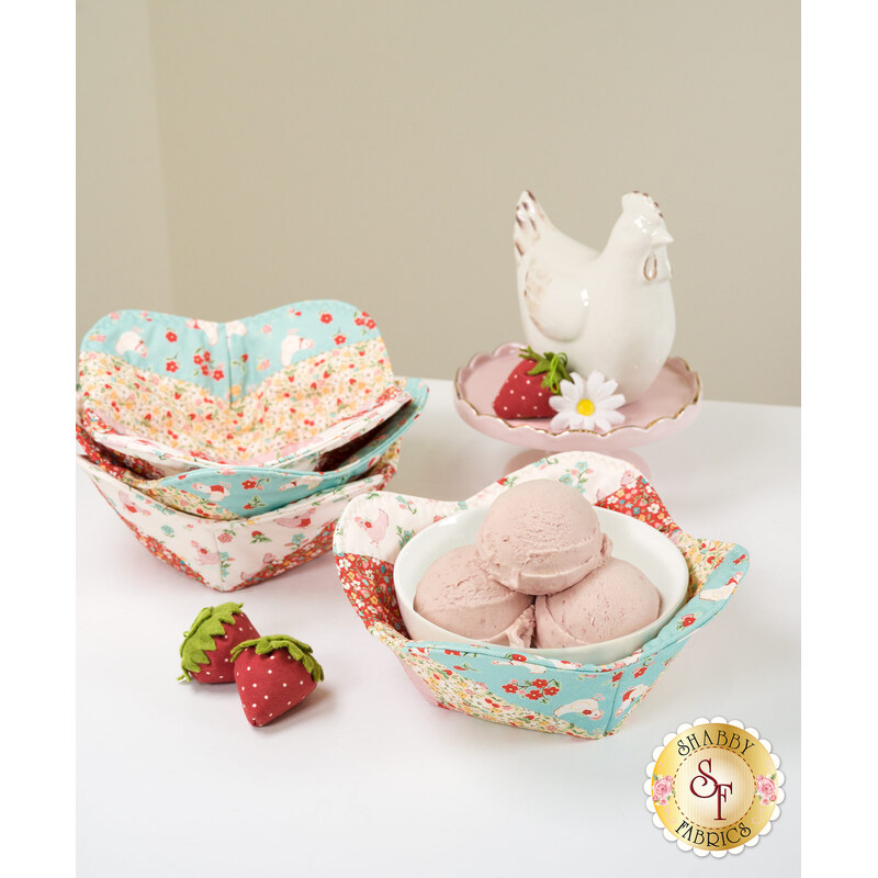 The completed Bowl Cozy's colored in blue, pink, red, and white vintage inspired fabrics from the Farmhouse Fancy collection by Poppie Cotton, on a white table with a bowl of strawberry ice cream and coordinating décor.