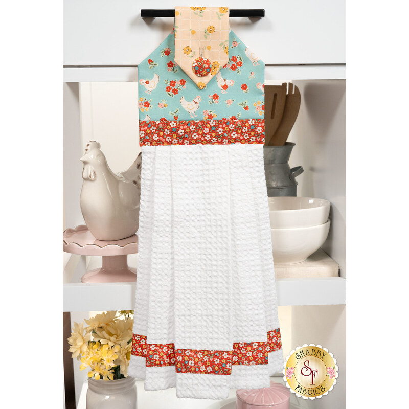 The completed Hanging Towel Kit colored in red, teal and yellow vintage floral fabrics from the Farmhouse Fancy collection by Poppie Cotton, hung on a drawer surrounded by coordinating décor. 