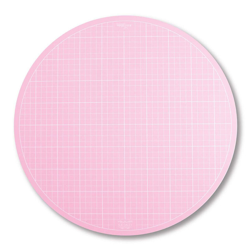 A round, pink cutting mat with a grid pattern for precise measurements and cutting.