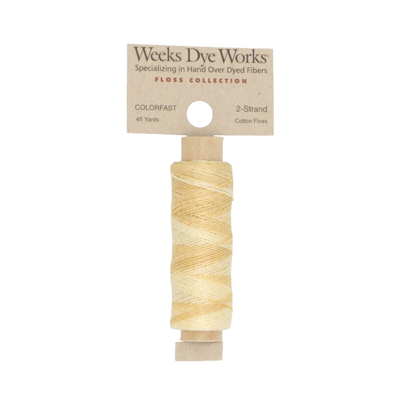A spool of butter yellow embroidery floss with a tan label featuring the brand name and color information.