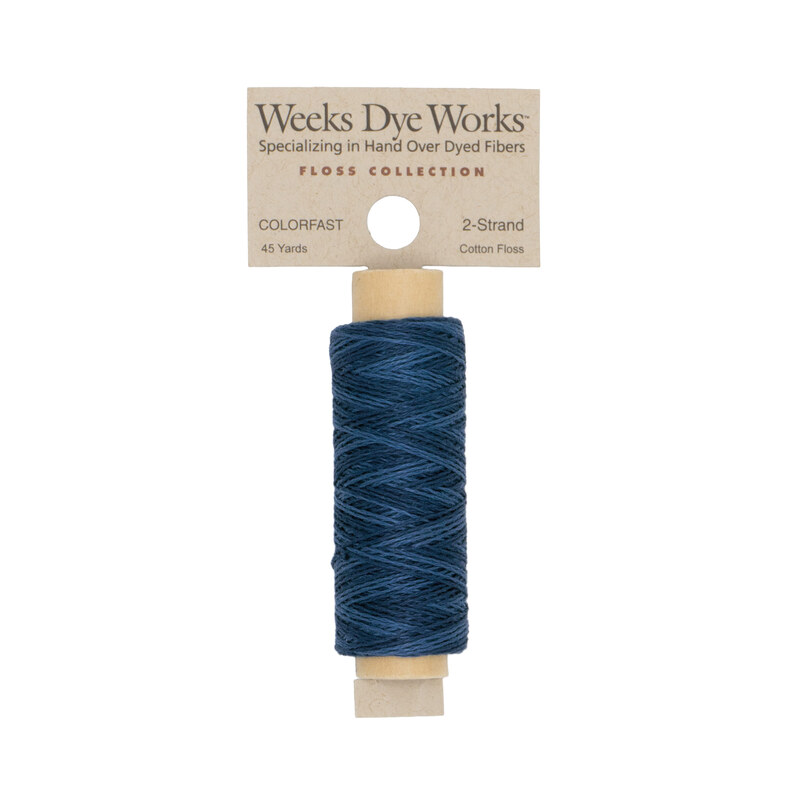 A spool of dark blue embroidery floss with a tan label featuring the brand name and color information.