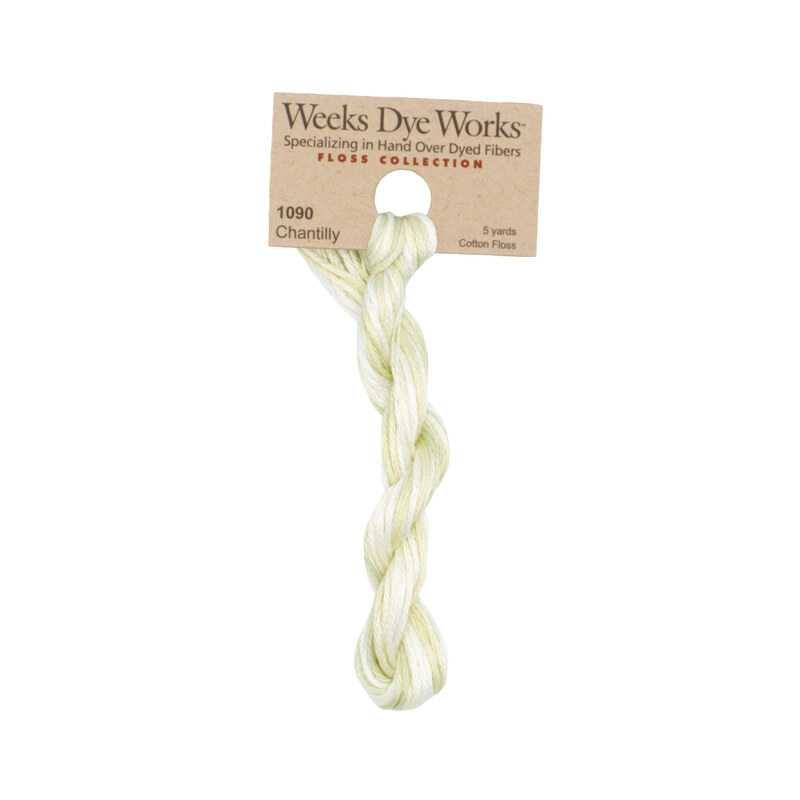 A skein of variegated pale celery and white embroidery floss, twisted and bundled, with a tan label featuring the brand name and color information.