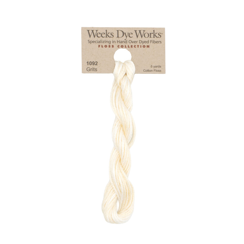 A skein of pale cream embroidery floss, twisted and bundled, with a tan label featuring the brand name and color information.