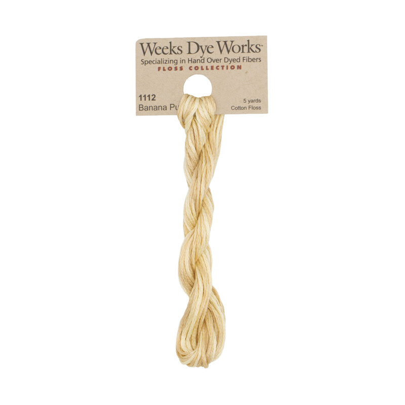 A skein of buff yellow embroidery floss, twisted and bundled, with a tan label featuring the brand name and color information.