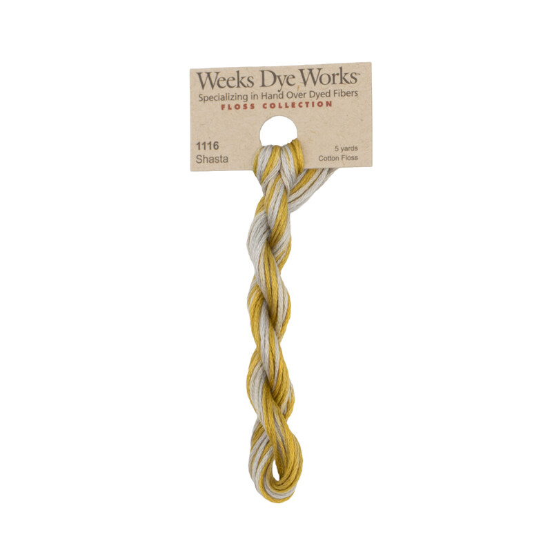 A skein of variegated dark gold and gray embroidery floss, twisted and bundled, with a tan label featuring the brand name and color information.
