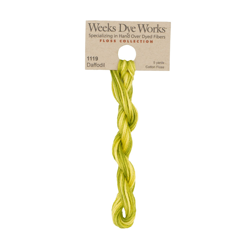 A skein of spring green and yellow embroidery floss, twisted and bundled, with a tan label featuring the brand name and color information.