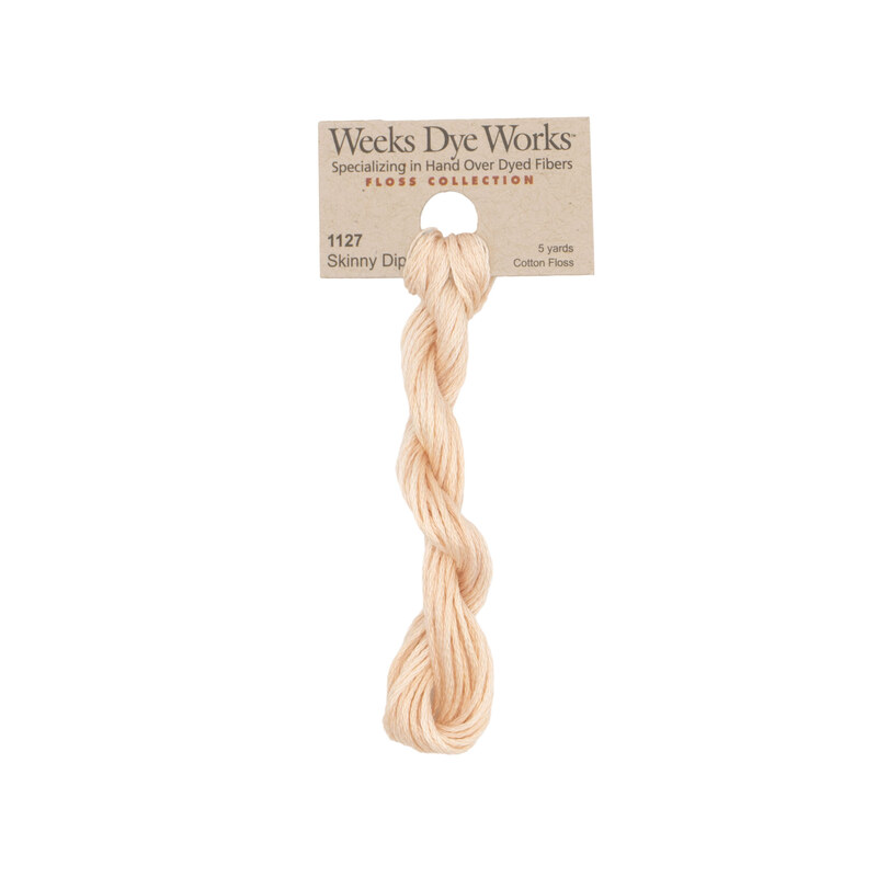 A skein of pale peach embroidery floss, twisted and bundled, with a tan label featuring the brand name and color information.
