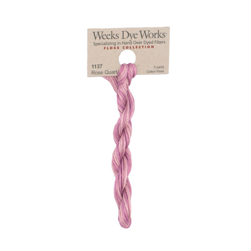 A skein of mauve pink embroidery floss, twisted and bundled, with a tan label featuring the brand name and color information.