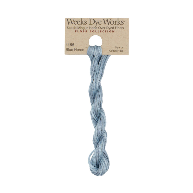A skein of light gray blue embroidery floss, twisted and bundled, with a tan label featuring the brand name and color information.