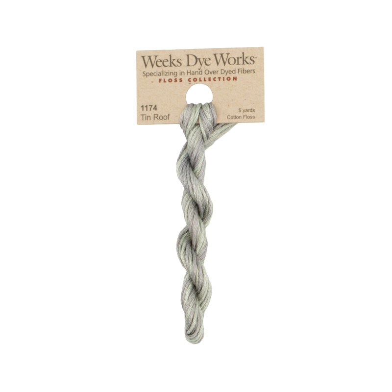 A skein of weathered gray embroidery floss, twisted and bundled, with a tan label featuring the brand name and color information.