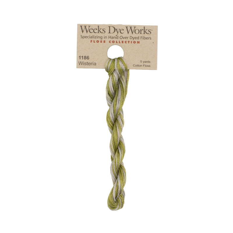 A skein of green and silver embroidery floss, twisted and bundled, with a tan label featuring the brand name and color information.