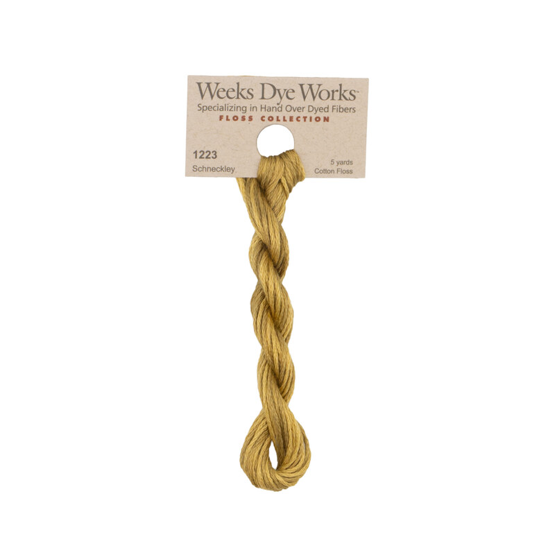 A skein of brass embroidery floss, twisted and bundled, with a tan label featuring the brand name and color information.