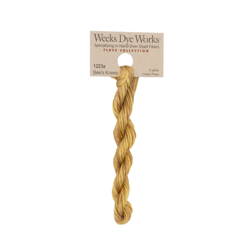 A skein of brassy yellow embroidery floss, twisted and bundled, with a tan label featuring the brand name and color information.