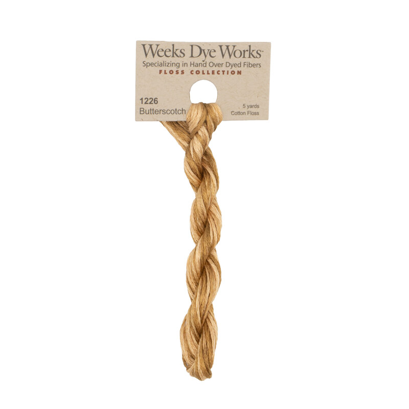 A skein of variegated bronze embroidery floss, twisted and bundled, with a tan label featuring the brand name and color information.