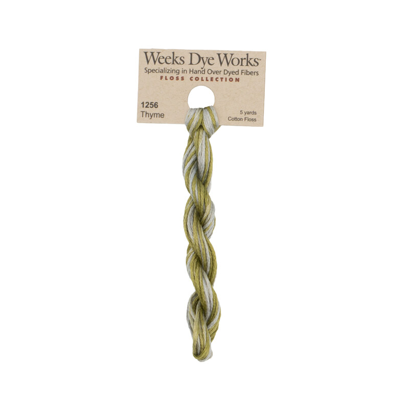 A skein of variegated olive green and gray embroidery floss, twisted and bundled, with a tan label featuring the brand name and color information.
