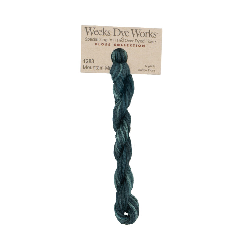 A skein of tonal, phthalo green embroidery floss, twisted and bundled, with a tan label featuring the brand name and color information.