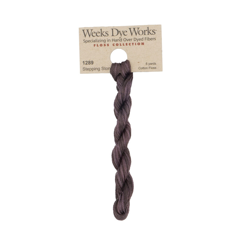 A skein of purple gray embroidery floss, twisted and bundled, with a tan label featuring the brand name and color information.