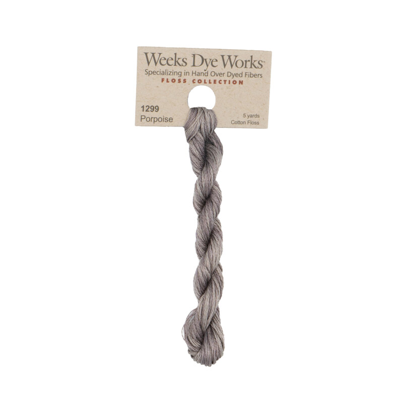 A skein of warm gray embroidery floss, twisted and bundled, with a tan label featuring the brand name and color information.