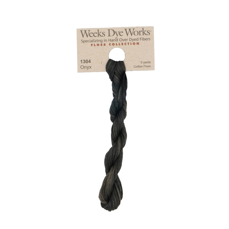 A skein of variegated coal black embroidery floss, twisted and bundled, with a tan label featuring the brand name and color information.