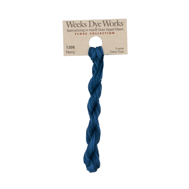 A skein of navy blue embroidery floss, twisted and bundled, with a tan label featuring the brand name and color information.