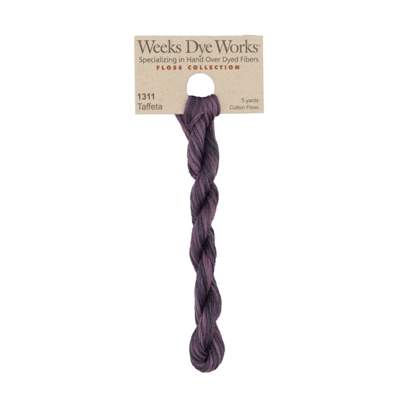 A skein of variegated plum purple embroidery floss, twisted and bundled, with a tan label featuring the brand name and color information.