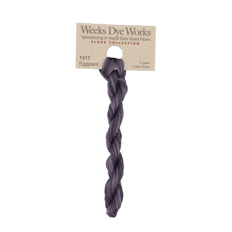 A skein of variegated, muted purple embroidery floss, twisted and bundled, with a tan label featuring the brand name and color information.
