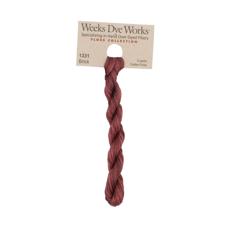 A skein of brick red embroidery floss, twisted and bundled, with a tan label featuring the brand name and color information.