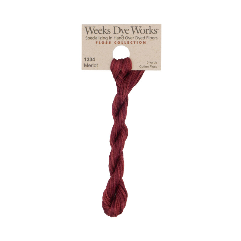 A skein of dark red embroidery floss, twisted and bundled, with a tan label featuring the brand name and color information.