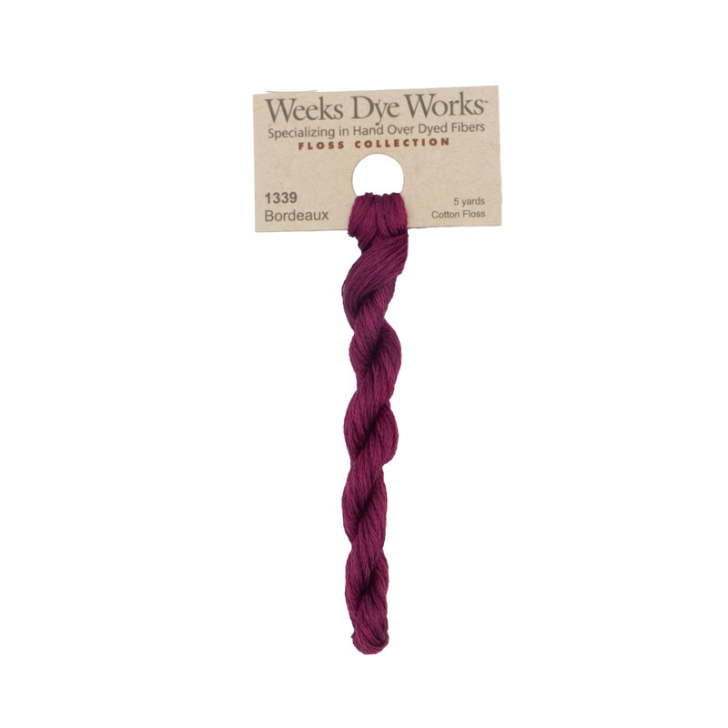 A skein of Dark Magenta embroidery floss, twisted and bundled, with a tan label featuring the brand name and color information.