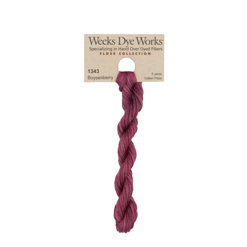 A skein of muted boysenberry red embroidery floss, twisted and bundled, with a tan label featuring the brand name and color information.