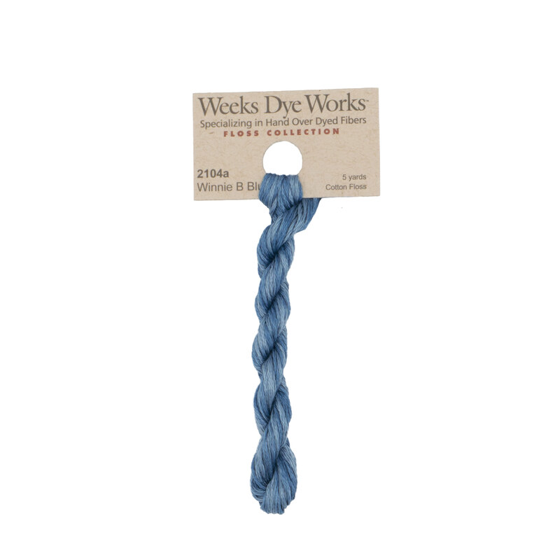 A skein of blue embroidery floss, twisted and bundled, with a tan label featuring the brand name and color information.