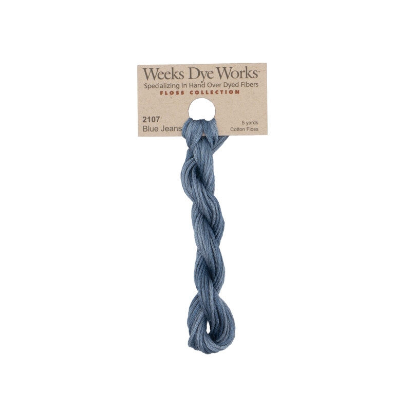 A skein of cadet blue embroidery floss, twisted and bundled, with a tan label featuring the brand name and color information.