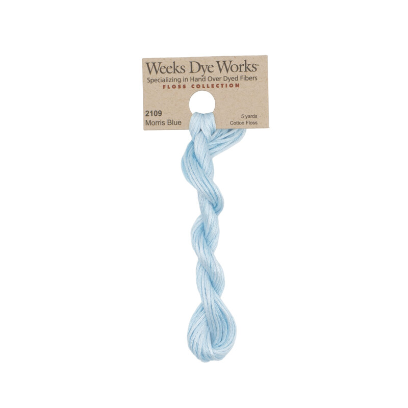 A skein of ice blue embroidery floss, twisted and bundled, with a tan label featuring the brand name and color information.