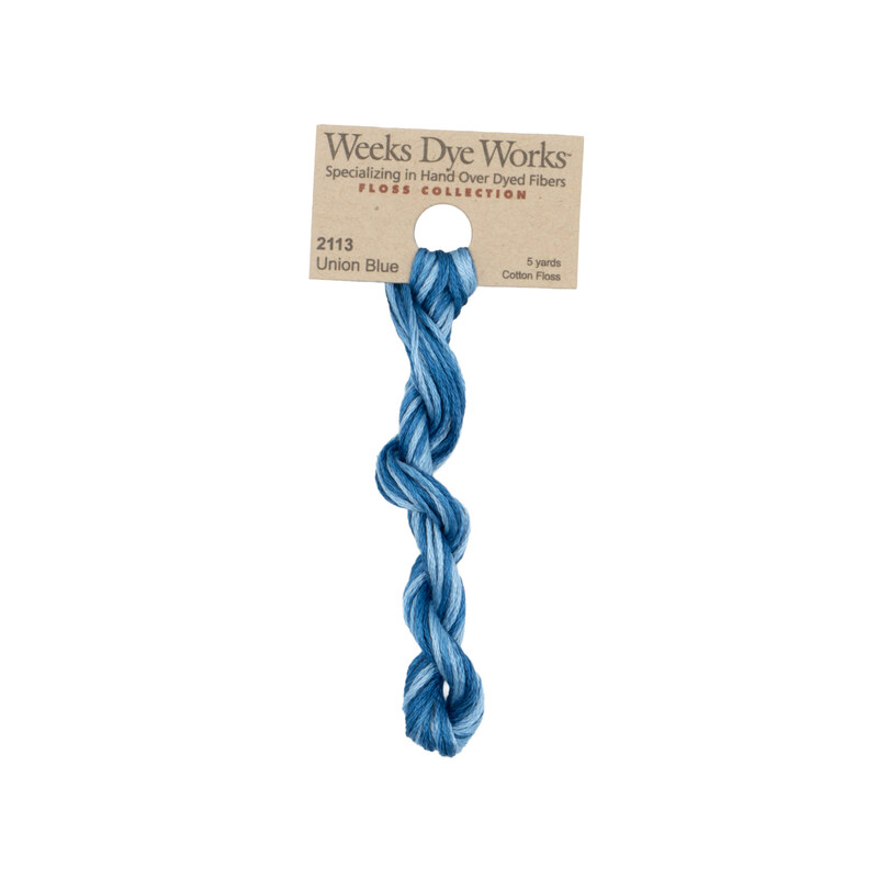 A skein of variegated blue embroidery floss, twisted and bundled, with a tan label featuring the brand name and color information.