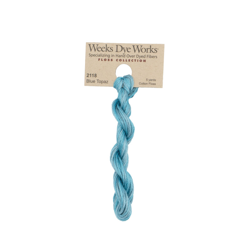 A skein of peacock blue embroidery floss, twisted and bundled, with a tan label featuring the brand name and color information.