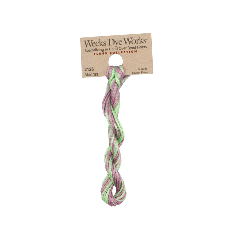 A skein of variegated light orchid and aqua embroidery floss, twisted and bundled, with a tan label featuring the brand name and color information.