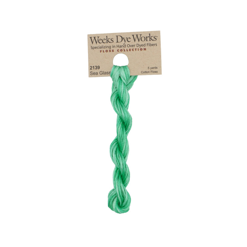A skein of seafoam green embroidery floss, twisted and bundled, with a tan label featuring the brand name and color information.