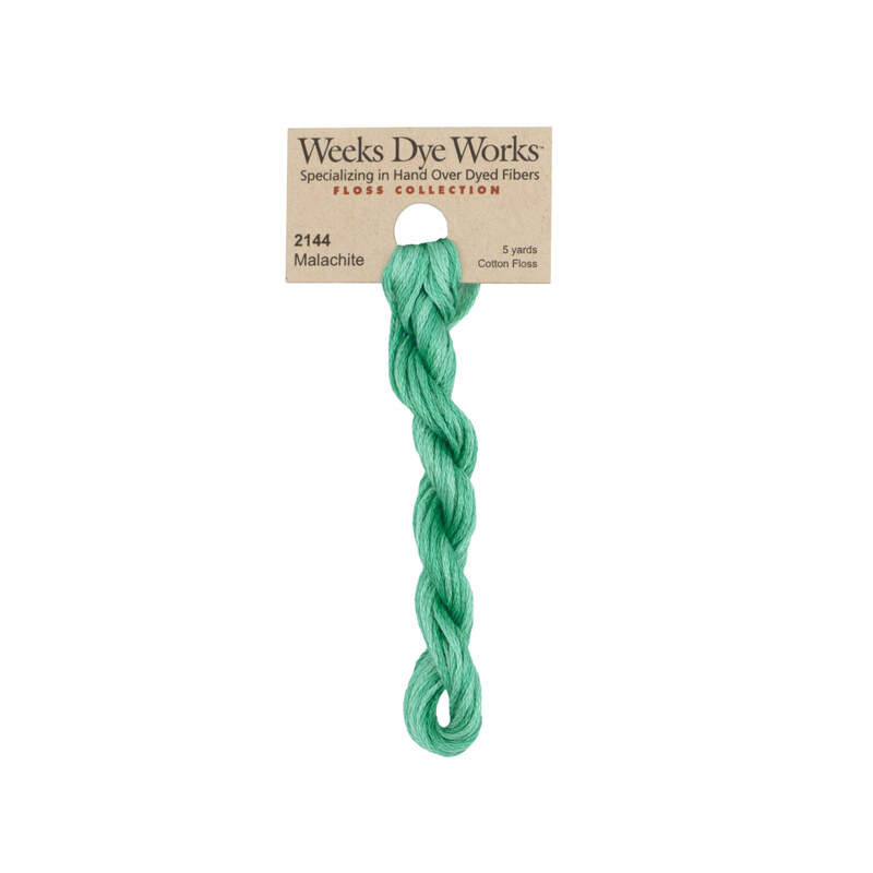 A skein of malachite embroidery floss, twisted and bundled, with a tan label featuring the brand name and color information.