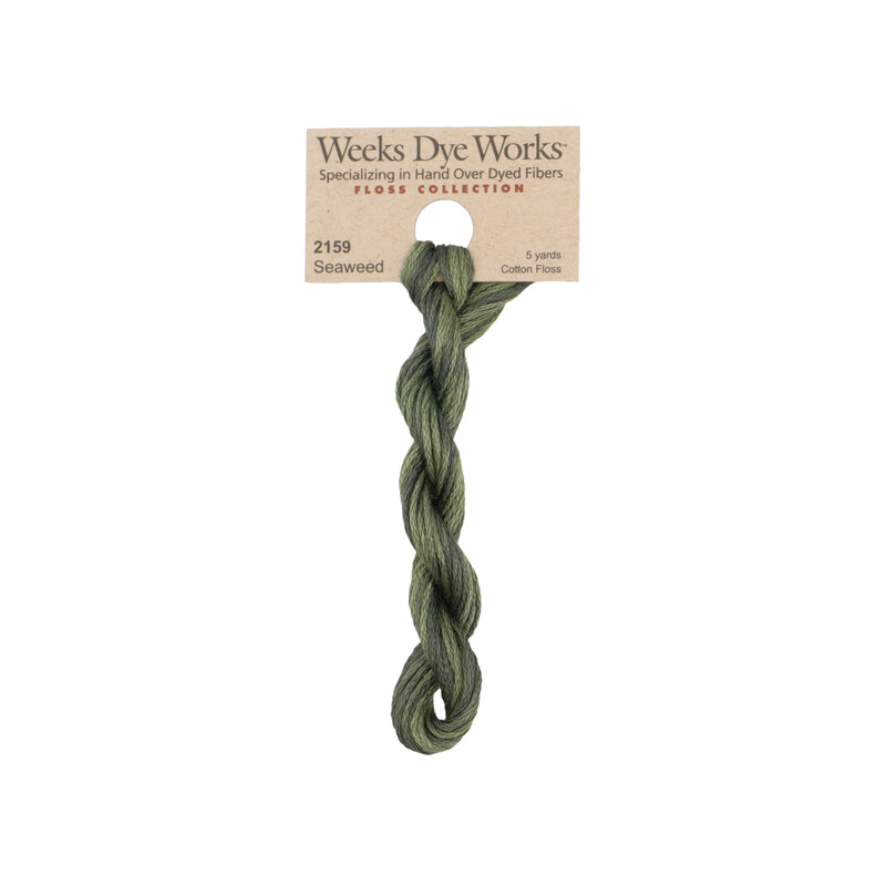 A skein of variegated forest green embroidery floss, twisted and bundled, with a tan label featuring the brand name and color information.