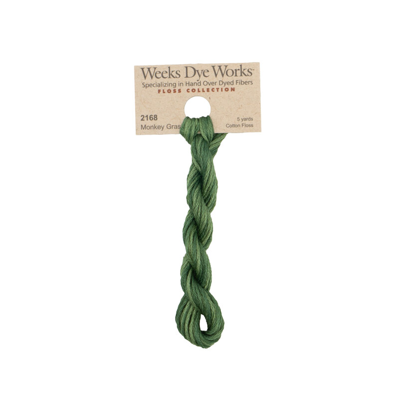 A skein of forest green embroidery floss, twisted and bundled, with a tan label featuring the brand name and color information.