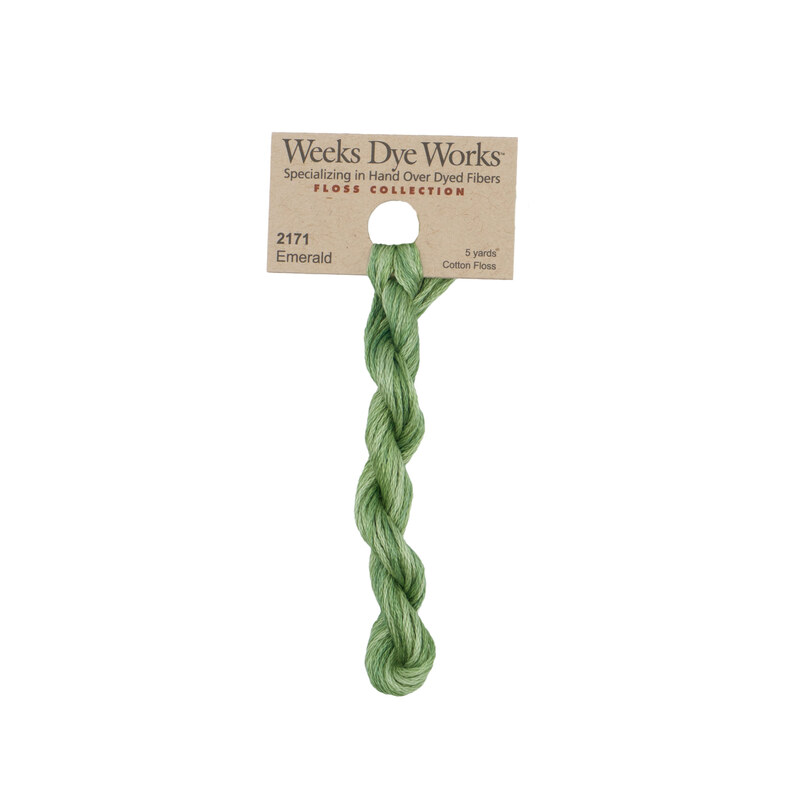 A skein of variegated grass green and pistachio embroidery floss, twisted and bundled, with a tan label featuring the brand name and color information.