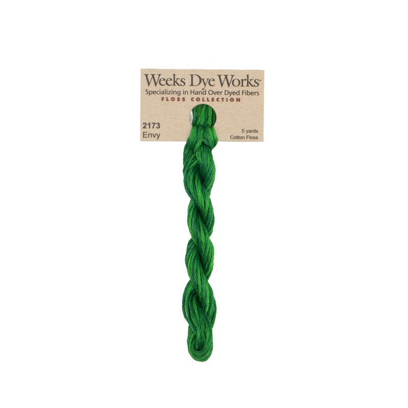A skein of forest green embroidery floss, twisted and bundled, with a tan label featuring the brand name and color information.