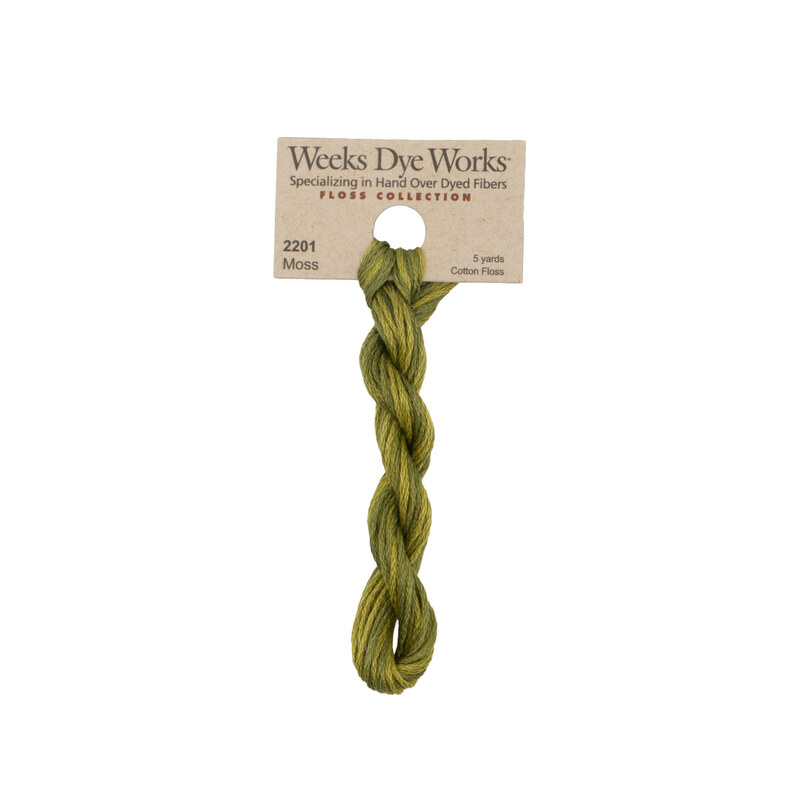 A skein of moss green embroidery floss, twisted and bundled, with a tan label featuring the brand name and color information.