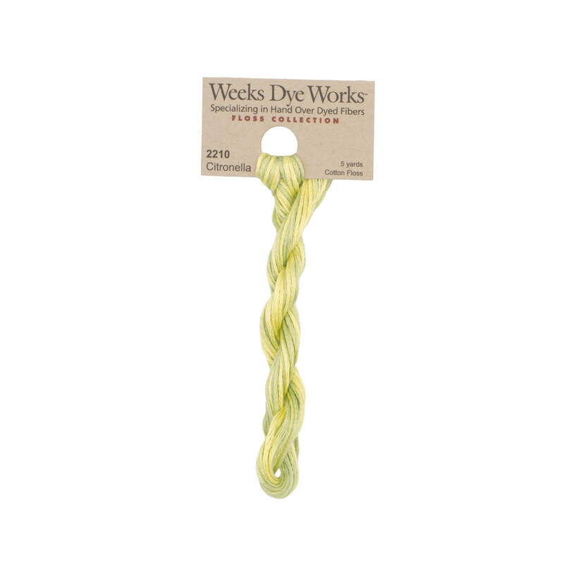 A skein of variegated light sage and pear embroidery floss, twisted and bundled, with a tan label featuring the brand name and color information.