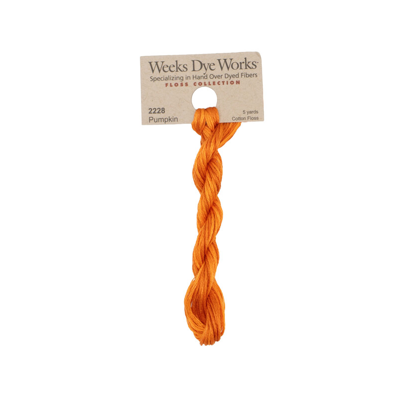 A skein of pumpkin orange embroidery floss, twisted and bundled, with a tan label featuring the brand name and color information.