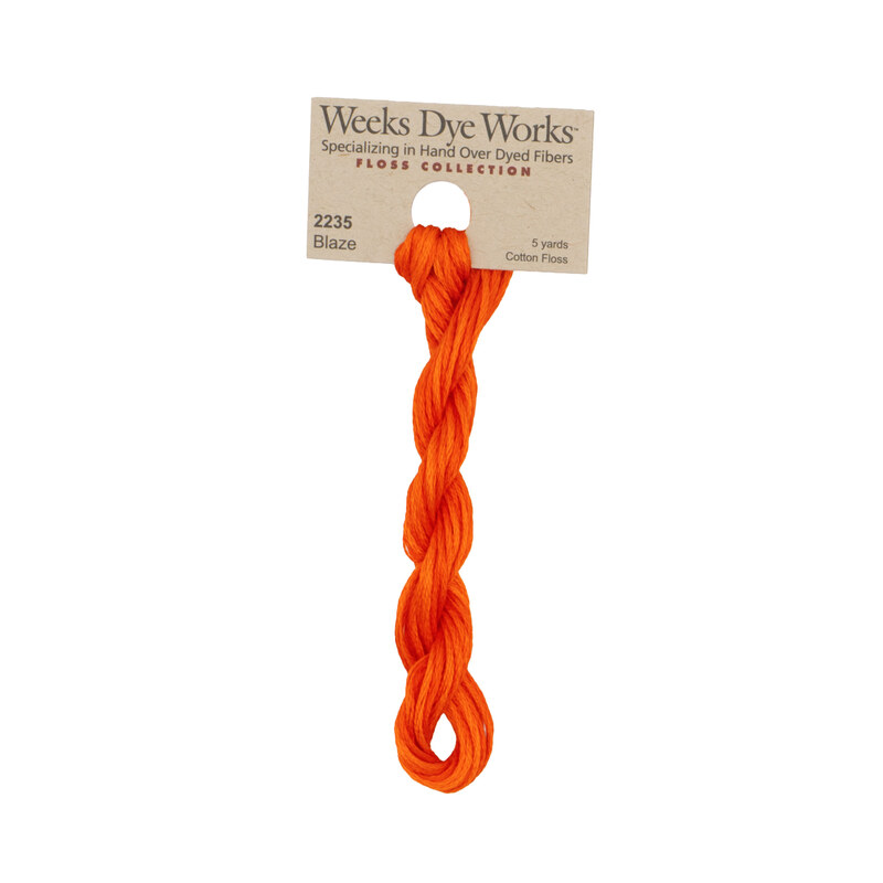 A skein of scarlet embroidery floss, twisted and bundled, with a tan label featuring the brand name and color information.