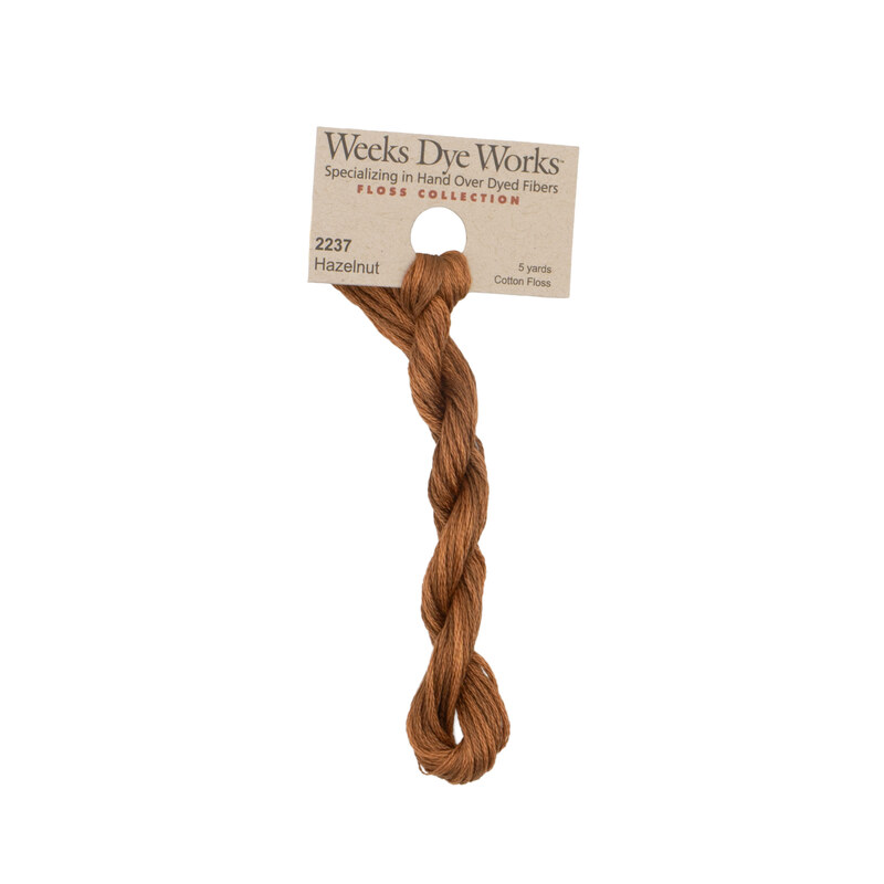 A skein of hazelnut brown embroidery floss, twisted and bundled, with a tan label featuring the brand name and color information.